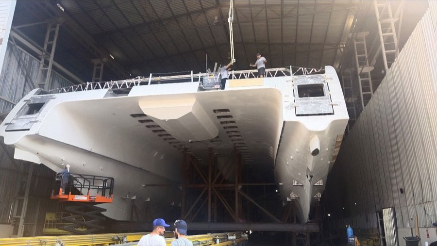 An unpainted aluminum hull suspended in a fabrication hall.